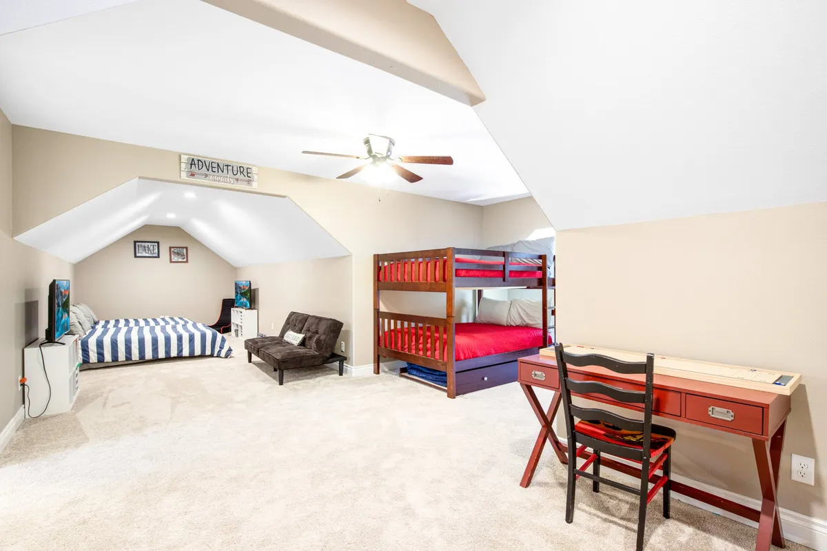 A playful loft-style bedroom designed for kids or additional guests, featuring bunk beds with striped bedspreads, a red desk for creative activities, and a futon for lounging or extra sleeping space. The room has a cheerful, cozy vibe that invites relaxation and fun.
