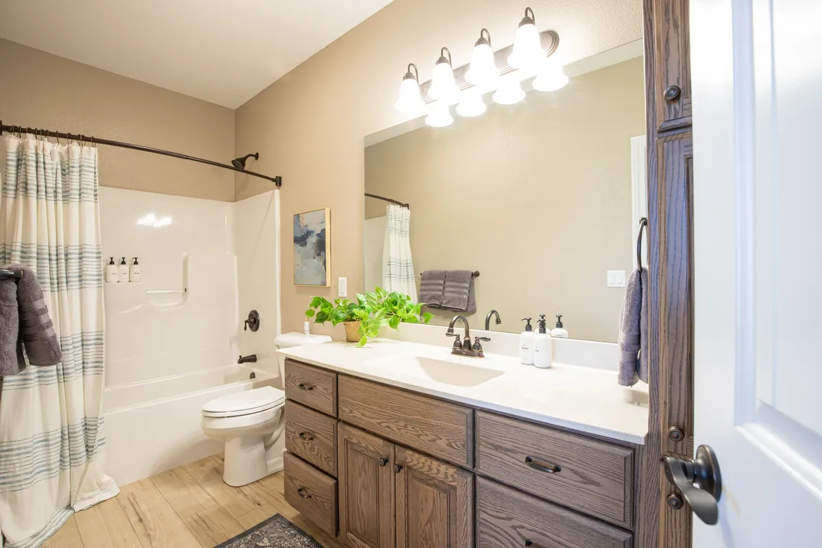 A serene ensuite bathroom with a double sink vanity, large framed mirror, bathtub, plush towels, and a refreshing green plant. The space is bathed in soft light, emphasizing both luxury and functionality for extended stays.