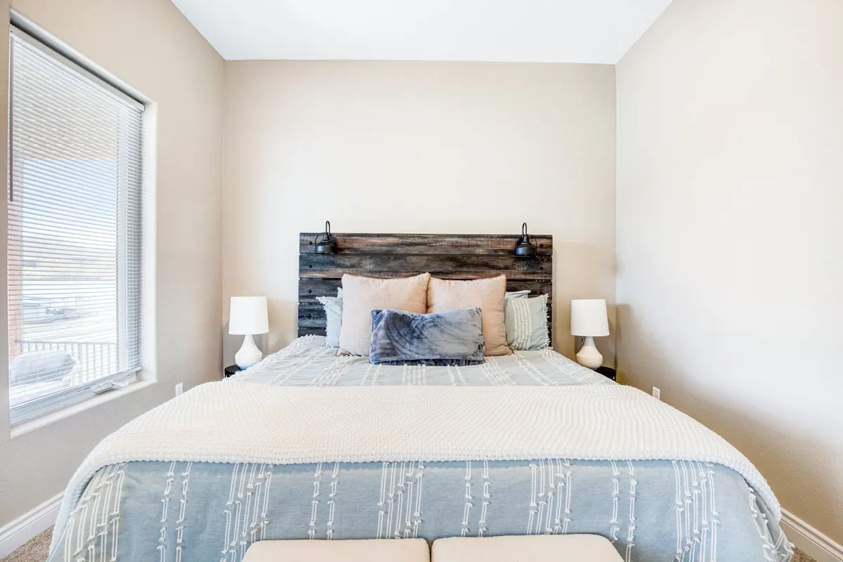 A king bedroom with a wooden headboard, decorative pillows, and nightstands topped with elegant lamps. Soft natural light fills the space, creating a tranquil and cozy atmosphere ideal for restful sleep. The serene colors and lake-inspired décor evoke a sense of peace and relaxation.