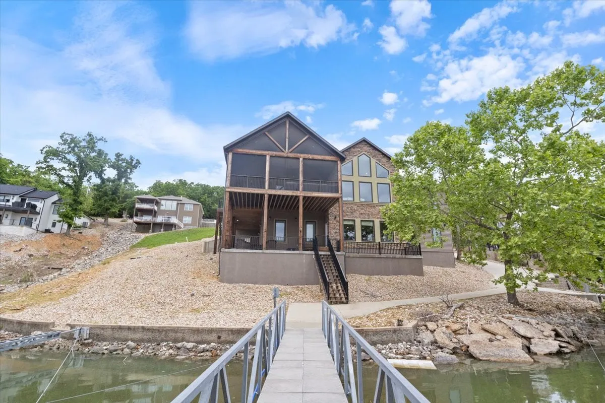 A wide shot of the modern lakefront cabin shows an expansive deck leading down to the water. The scene captures the connection between the home and the lake, with clear access to boating, fishing, and relaxing by the water—perfect for gathering after an active day on the lake.