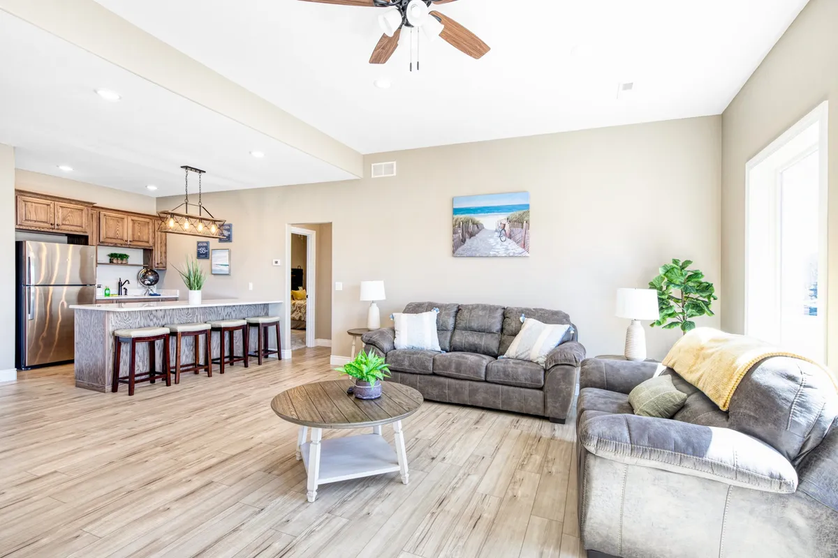 A versatile social space where a comfortable living area flows into the kitchen, featuring a kitchen island, artwork, lush plants, and cozy seating. The design encourages both cooking and conversation, perfect for casual get-togethers or relaxed entertaining.