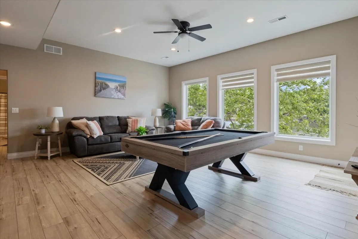 A bright, casual lower-level living space highlighted by a pool table, comfortable sofa, and large windows. The area is ideal for games and relaxed socializing, bathed in natural light and arranged for both activity and relaxation.