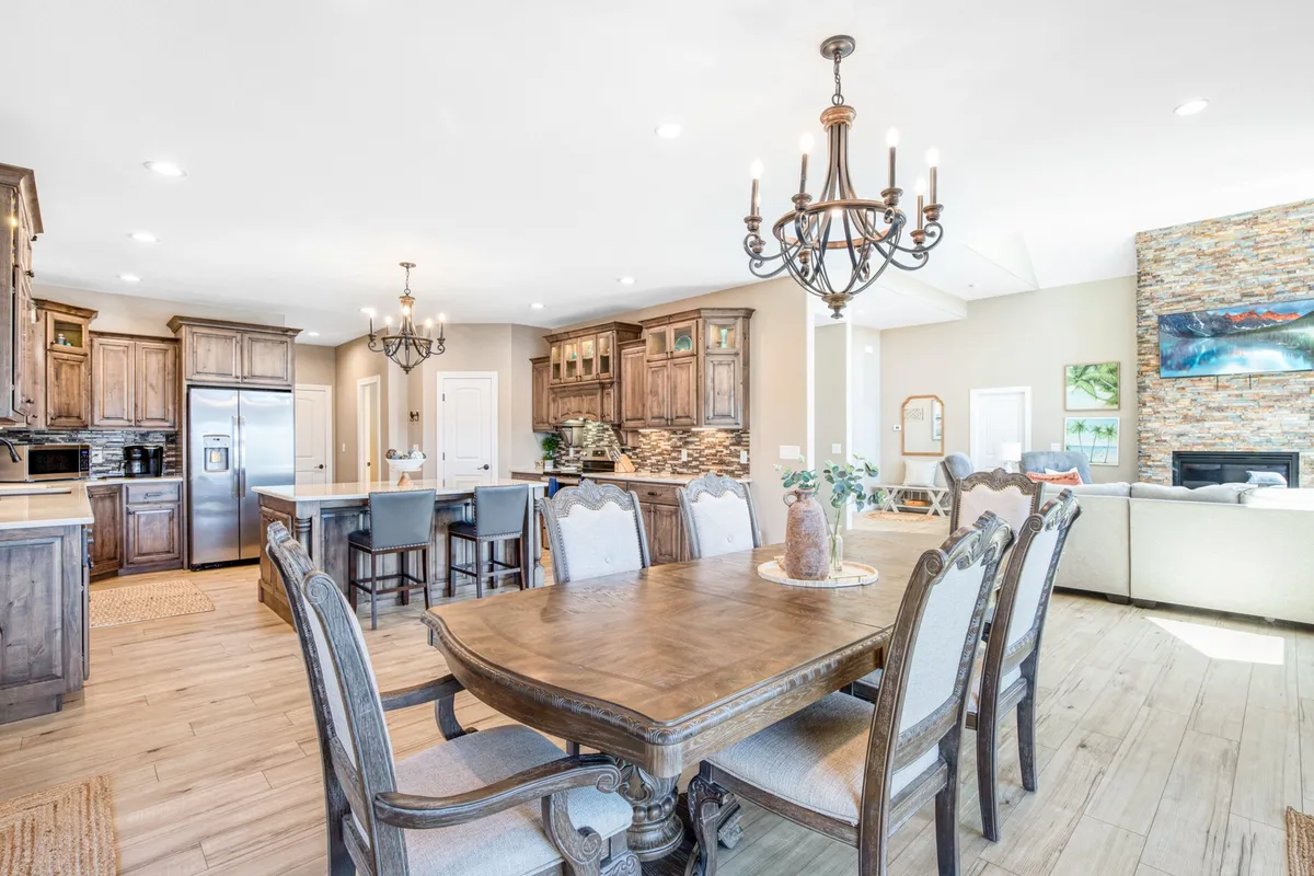 A cozy dining area seamlessly connected to the kitchen, featuring a generous dining table, a classic chandelier, stylish cabinetry, and a striking stone fireplace. The ambiance is warm and welcoming, designed for family meals, entertaining, and special celebrations.