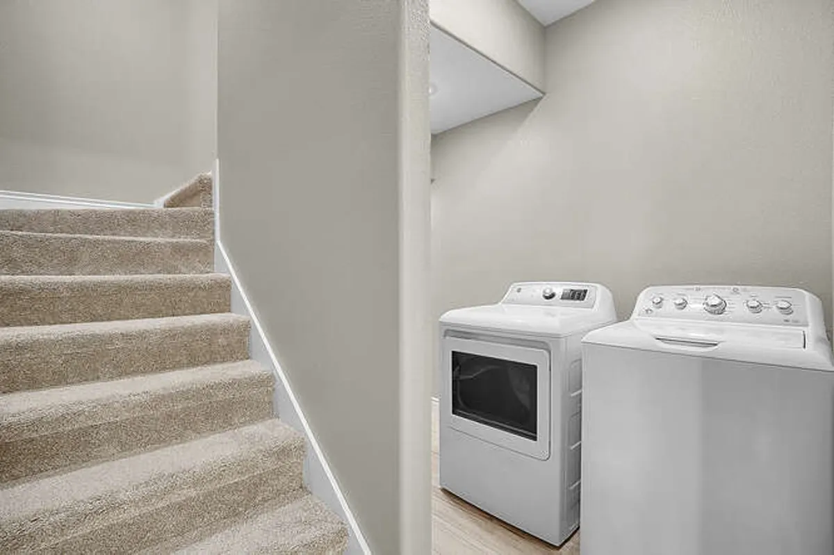 A light-filled laundry area at the base of a staircase, featuring a modern washer and dryer. The space is practical and organized, ideal for guests looking for extended-stay convenience and fresh linens throughout their visit.